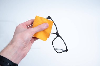 Açık arkaplanda kusursuz berraklık için siyah gözlük lenslerini yumuşak sarı kumaşla dikkatlice siliyorum..