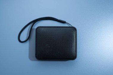 Küçük siyah taşınabilir bluetooth hoparlörü, delinmiş ızgarası ve siyah kayışı var.