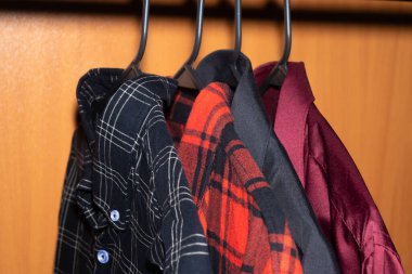 Ahşap gardıroptaki askılarda farklı renklerde birkaç ekose gömlek asılı..