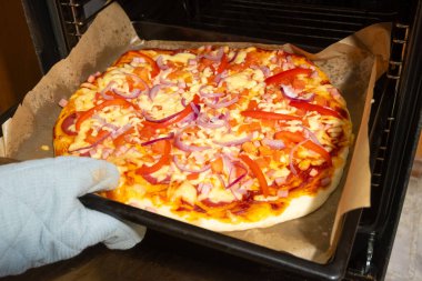 Peynirli, biberli, soğanlı ve jambonlu iştah açıcı pizza sıcak fırında, servis için hazır..