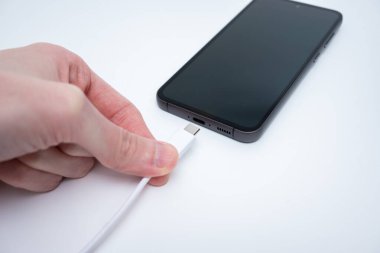 Bir el, modern teknolojinin gelişimini gösteren şarj kablosuna bağlı bir telefonu tutuyor..