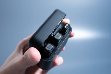 El ele tutuşan siyah şarj çantası, ışık arka planında kablosuz kulaklıkları ortaya çıkarıyor..