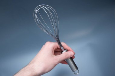 Erkek el paslanmaz çelik çırpıcıyı sıkıca kavrıyor, temiz ışık arka planında sallanıyor, kaliteyi ve yemek pişirme kolaylığını vurguluyor..