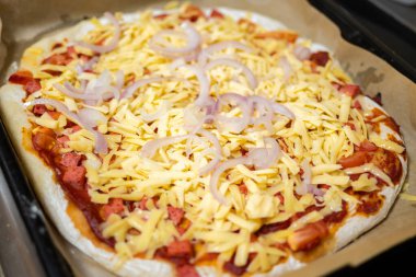 Fırına girmeden önce pizzanın üzerinde rendelenmiş peynir ve soğan halkaları..