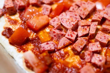 Napoli usulü ev yapımı pizza: sosis küpleri ve fırından önce taze domates.