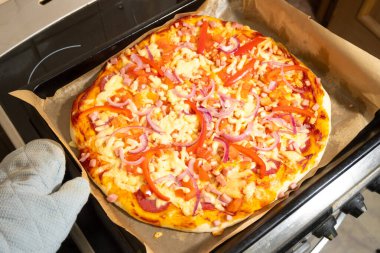 Eritilmiş peynirli taze sıcak pizza, biber ve parşömen üzerinde soğan..