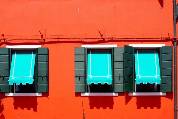 Três janelas com dossel azul em Burano na parede laranja vermelha — Fotografia de Stock