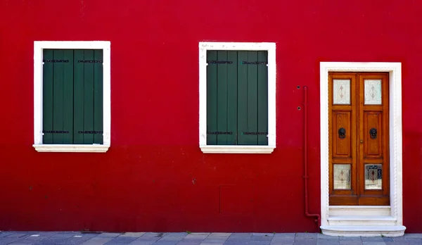 Porta de madeira e duas janelas na parede vermelha — Fotografia de Stock