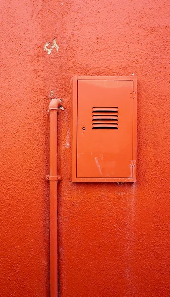 Vertical metal pipe and electric box on orange color wall — Stock Photo, Image