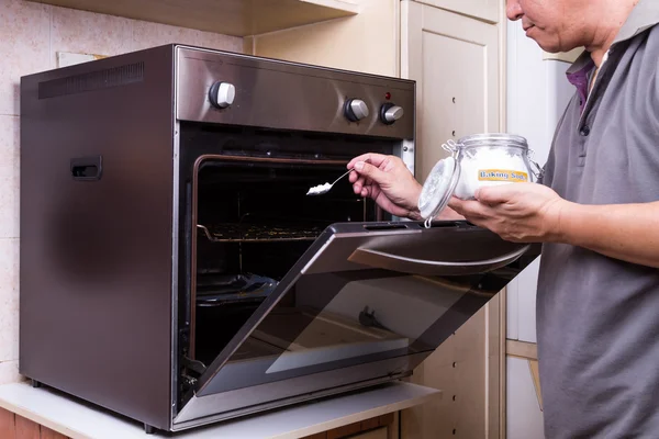 Человек, посыпающий пищевую соду в жирную печь в качестве чистящего средства — стоковое фото
