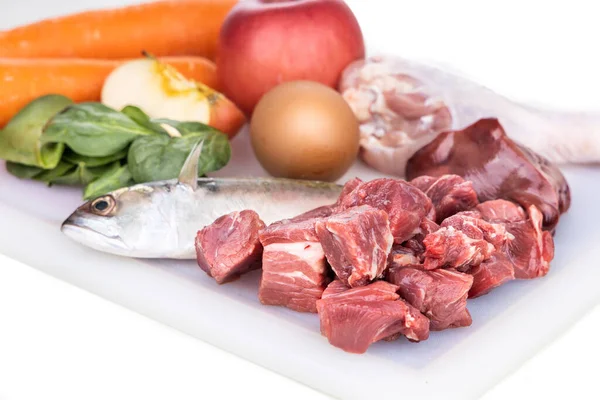 Primer plano de los ingredientes de la receta de comida cruda vómito para perros que consiste en carne, órganos, pescado, huevos y verduras en la tabla de picar —  Fotos de Stock