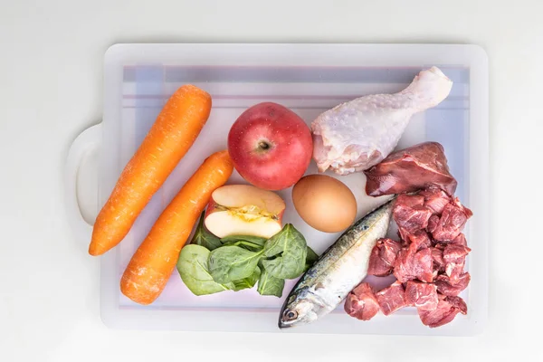 Visão geral dos ingredientes da receita de alimentos crus para cães que consistem em carne, órgãos, peixes, ovos e vegetais em tábua de cortar — Fotografia de Stock