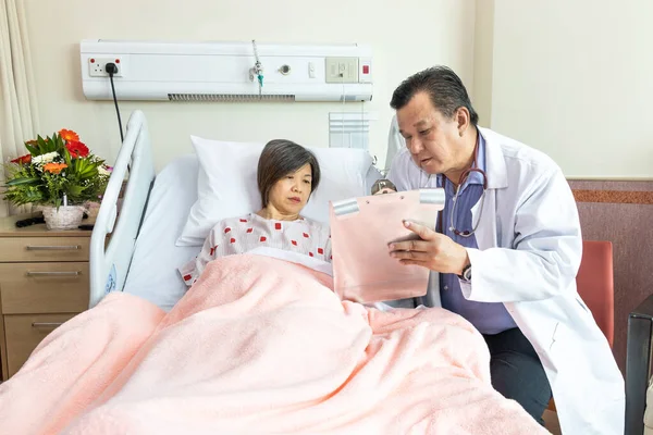 Confiado médico asiático explicando alegre paciente femenino en condición médica acostado en la cama en el hospital. —  Fotos de Stock