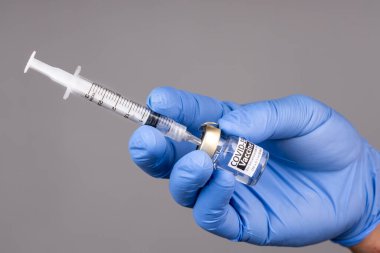 Eline cerrahi eldiven tak ve şırıngayı covid-19 aşı şişesine yerleştir.