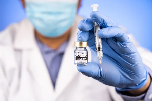 Close-up og fokus på Covid-19 vaccine hætteglas og sprøjte, som den asiatiske læge holder med medicinsk handske i baggrunden - Stock-foto