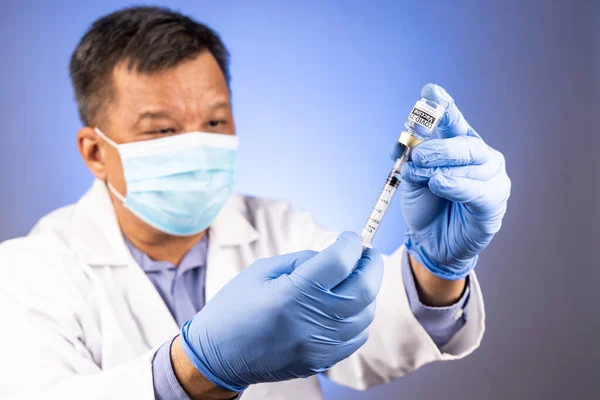 Close-up and focus on syringe inserted into Covid-19 vaccine vial by Asian medical doctor with medical glove in background — Stock Photo, Image