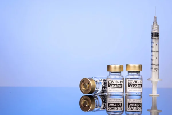 Botol vaksin Covid-19 dengan konsep jarum suntik pada permukaan reflektif pada latar belakang biru — Stok Foto