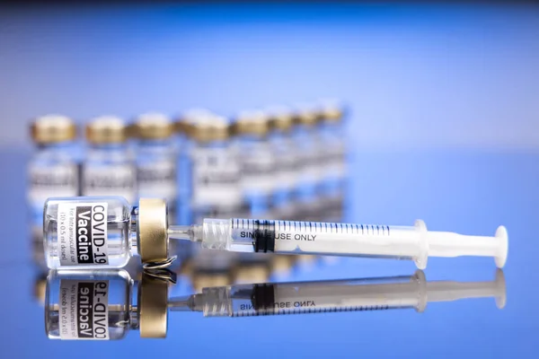 Suntikan yang dimasukkan ke dalam botol berisi konsep vaksin Covid-19 pada latar belakang biru — Stok Foto