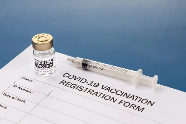 Covid-19 vaccination registration form with vial and syringe on blue desk