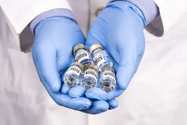 Close-up of both hands with surgical glove holding multiple covid-19 vaccine vial — Stock Photo, Image