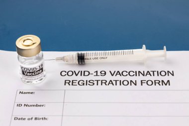 Covid-19 aşı kayıt formu mavi masa üzerinde şişe ve şırınga ile