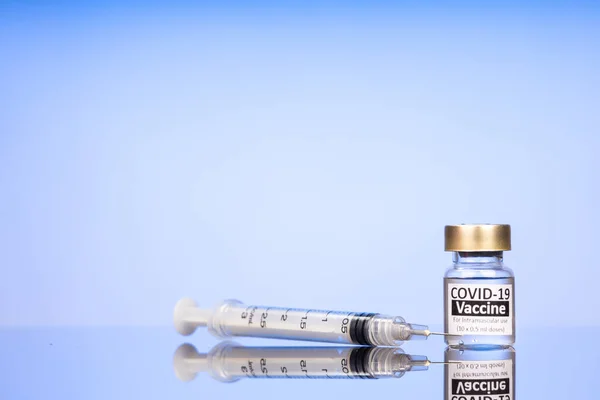 Covid-19 vaccine hætteglas med sprøjte koncept på reflekterende overflade på blå baggrund - Stock-foto