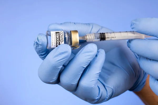 Close-up of hand with surgical glove insert syringe into covid-19 vaccine vial on blue background — Stock Photo, Image