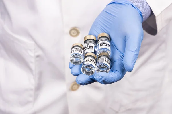 Close-up of hand with surgical glove holding multiple covid-19 vaccine vial — Stock Photo, Image