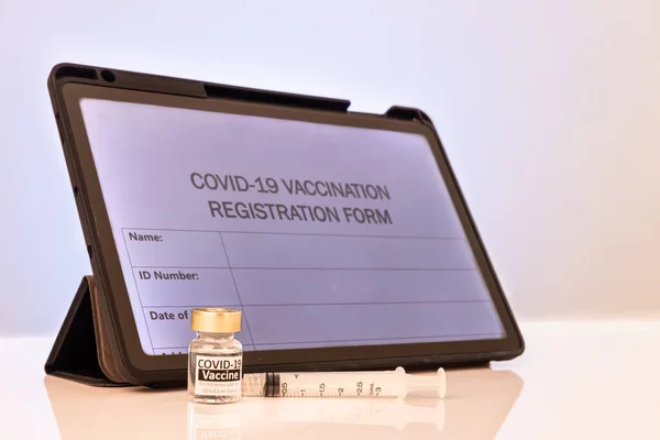 Covid-19 vaccination online registration form on computer tablet screen with vial and syringe as props on table