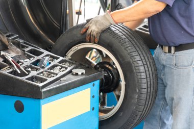Tamirci, atölyede tekerlek dengeleme sırasında uygun ağırlığı tekere takıyor
