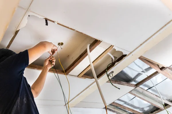 Eletricista escondendo linhas de fio de eletricidade electicidade dentro de tubo de plástico incorporado no teto. — Fotografia de Stock