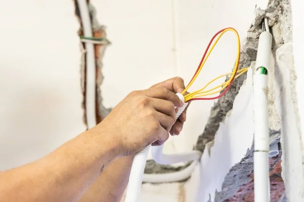 Eletricista escondendo linhas de fio de energia de eleticidade dentro do tubo de plástico incorporado na parede — Fotografia de Stock