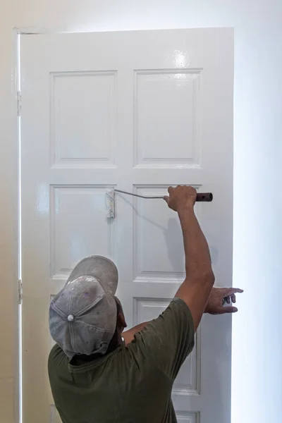 Person bemalt weiße Holztür mit Farbroller bei Renovierung des Hauses — Stockfoto