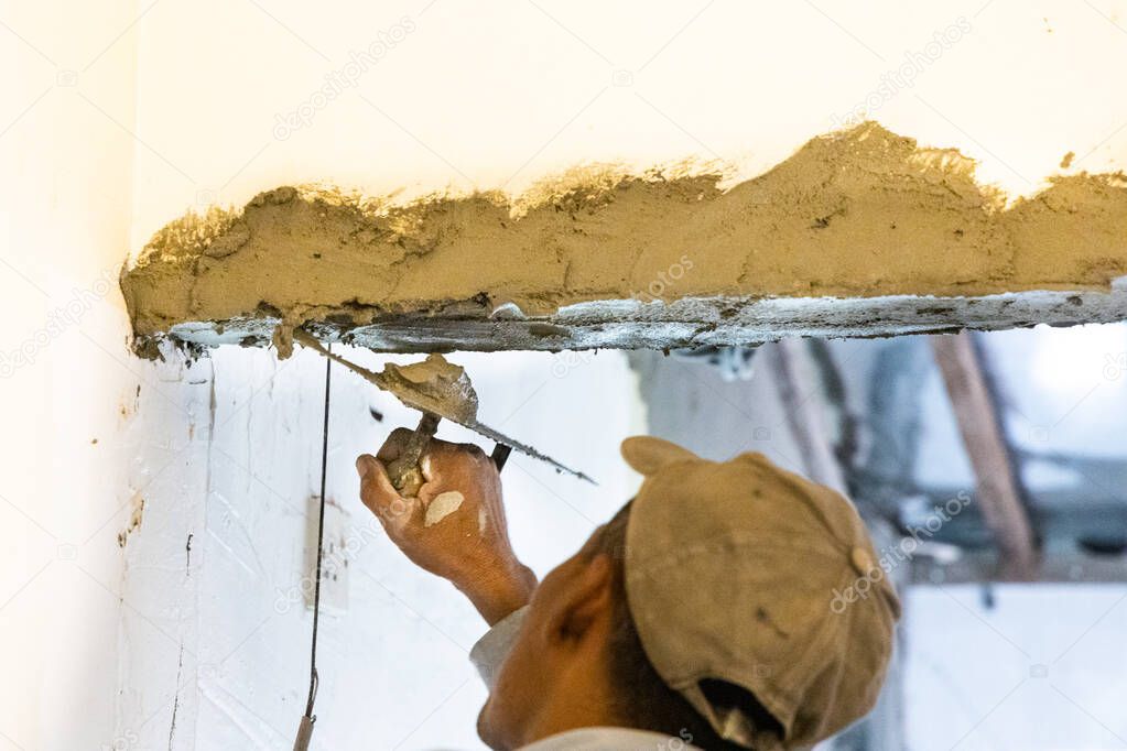 Worker plastering cement mortar on concrete ceiling beam with trowel