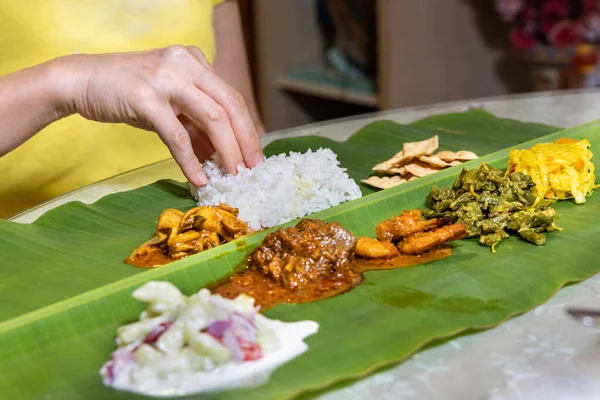 Person enjoying Indian banana leaf rice consisting mutton curry, squid, prawn, papadam and various vegetables — Stock Photo, Image