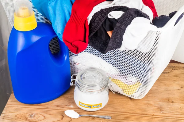 Baking soda with detergent and pile of dirty laundry. — Stock Photo, Image