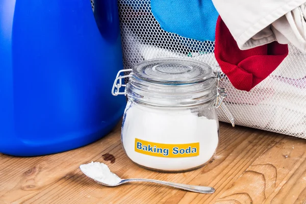 Baking soda with detergent and pile of dirty laundry. — Stock Photo, Image