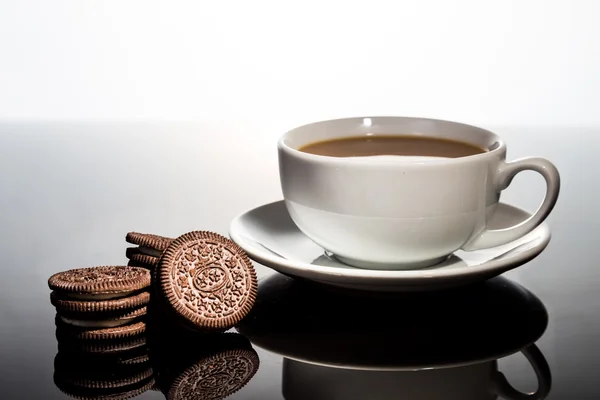 Creme-gefüllte Sandwich-Plätzchen und Tasse Kaffee auf dunklem, reflektierendem Hintergrund — Stockfoto