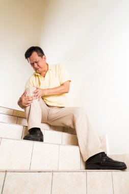Matured man suffering with acute knee joint pain seated on stairs clipart