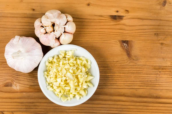 Chopped garlic in a plate with garlic bulb and cloves as background