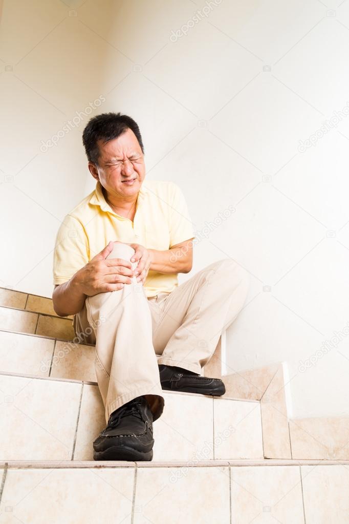 Matured man suffering with acute knee joint pain seated on stairs