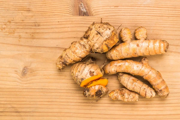 Fresh turmeric roots with wellness properties on wooden surface. — Stockfoto