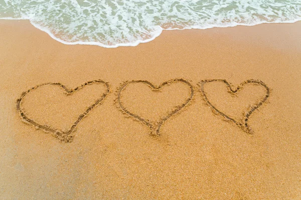 Tres Corazones dibujados en la playa de arena con olas acercándose — Foto de Stock