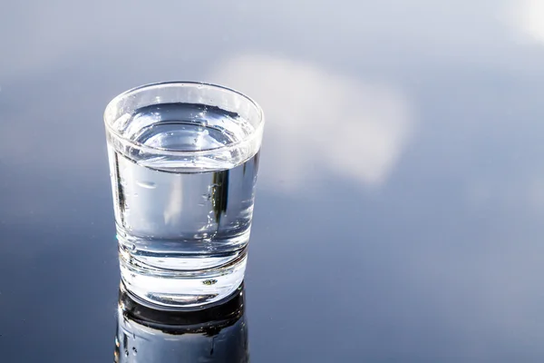 Refreshing water in transparent glass with reflection against blue sky — Stock Photo, Image