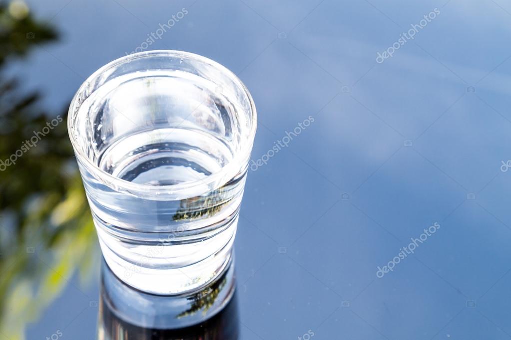 Refreshing water in transparent glass with reflection against blue sky