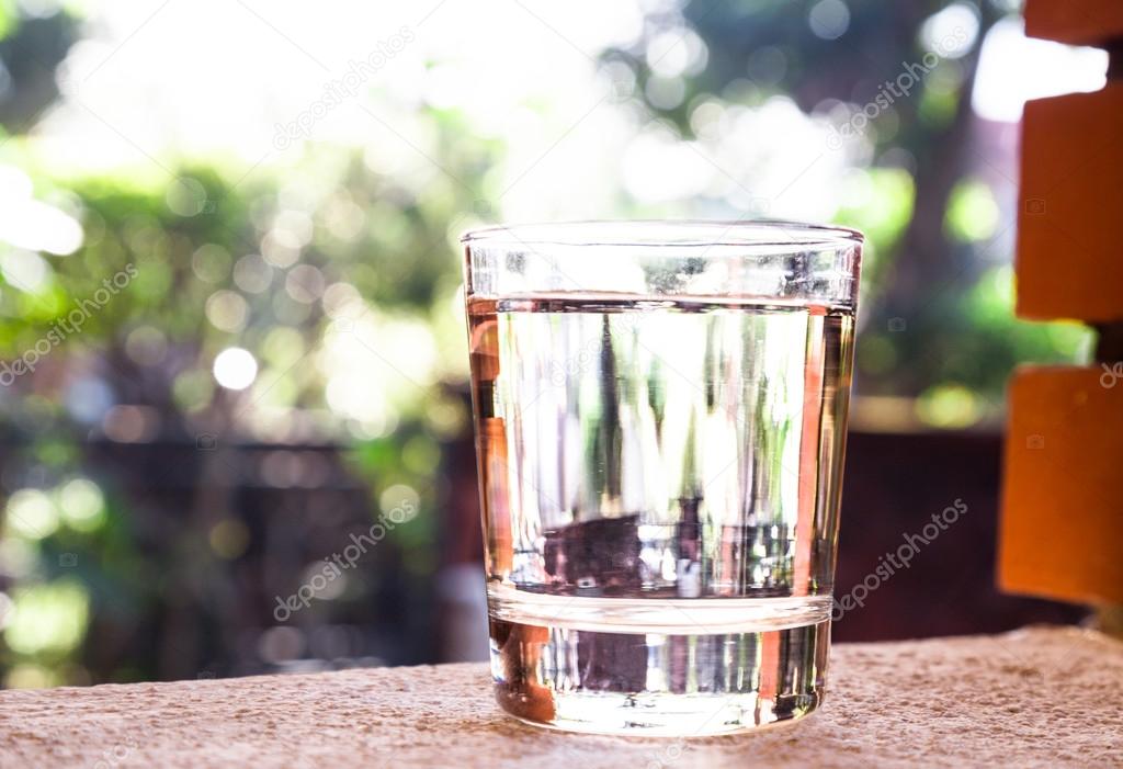Refreshing water in transparent glass  against with greeneries background