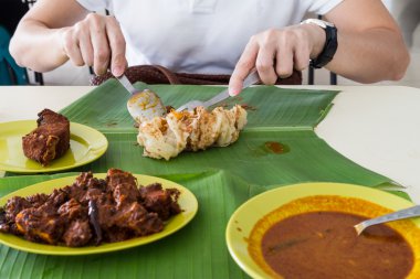 Person eating roti prata, masala mutton, fish on banana leaf