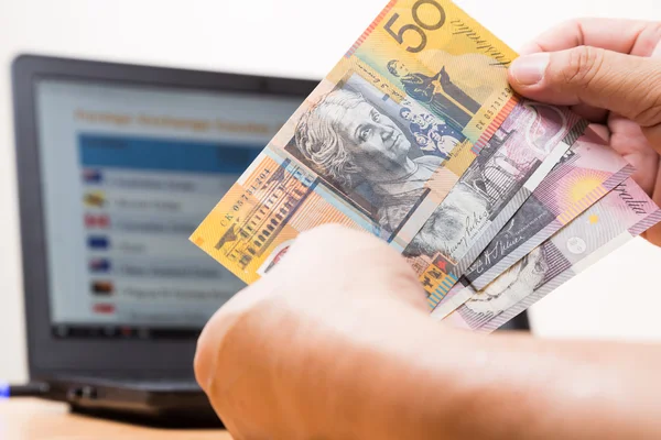 通貨交換表をコンピューターの画面上の前にオフィスにオーストラリアドルを持っている手. — ストック写真