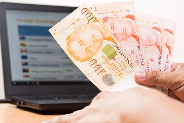 Hand met Singapore dollar in office voor valuta exchange grafiek op computerscherm. — Stockfoto