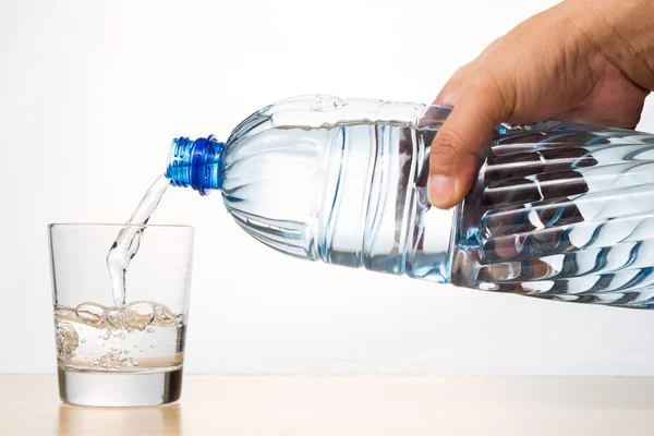 Main versant l'eau minérale naturelle rafraîchissante de la bouteille dans le verre — Photo